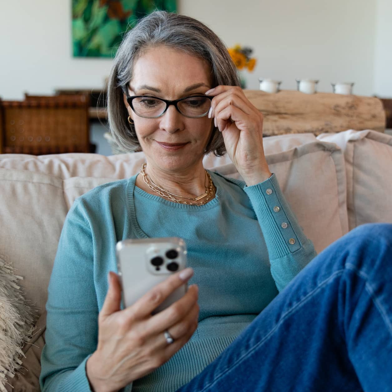 An older woman on her sofa, looking at her cell phone screen.