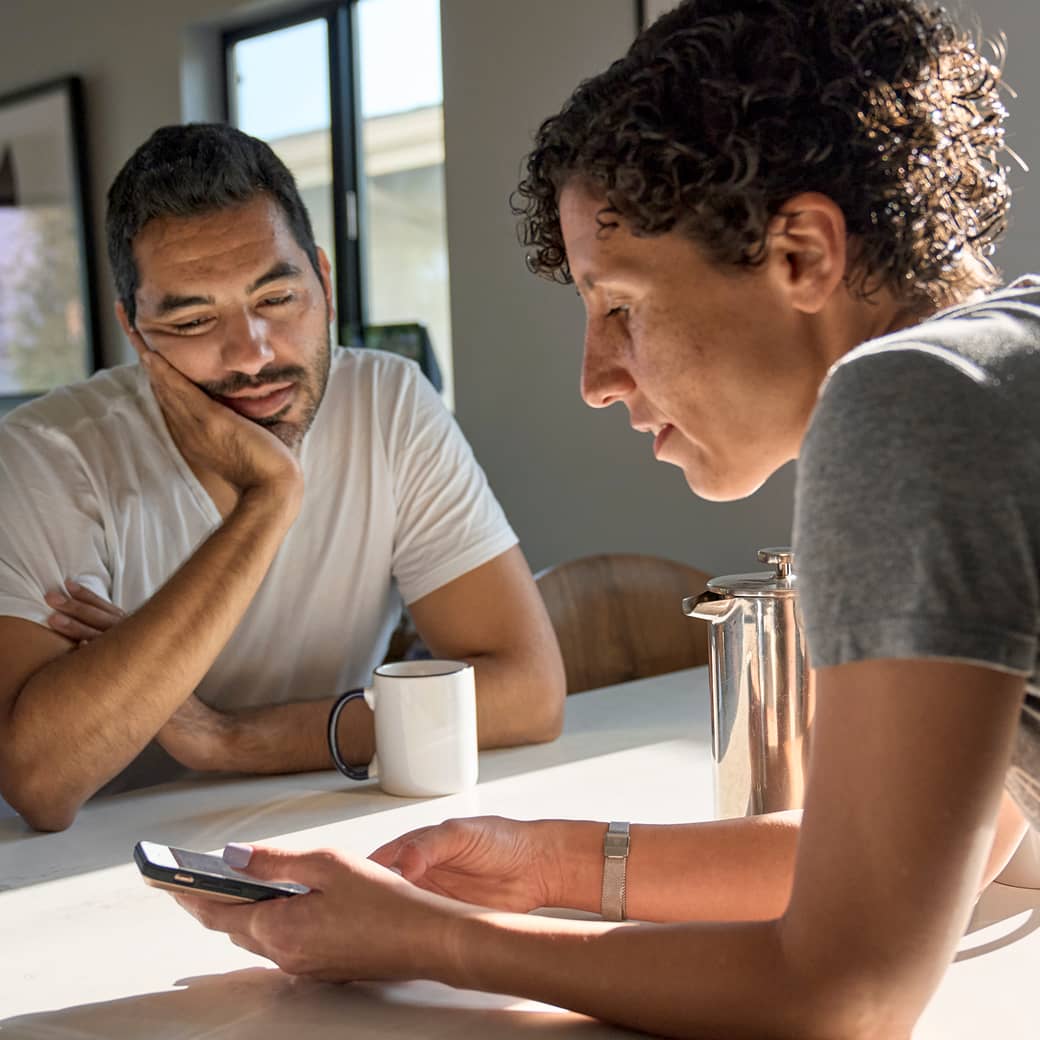 A couple looking at a cell phone screen in their kitchen.