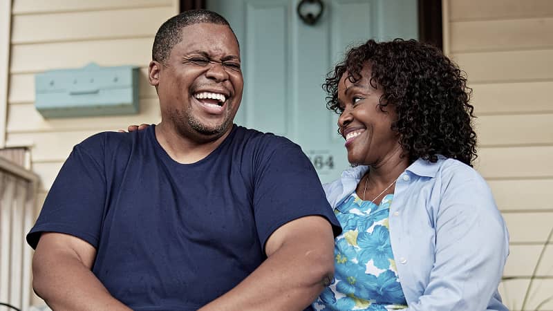 A couple laughing while waiting for a delivery on their front steps.