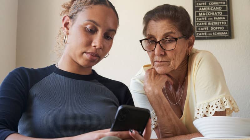 An older parent and young adult checking a prescription on a cell phone.
