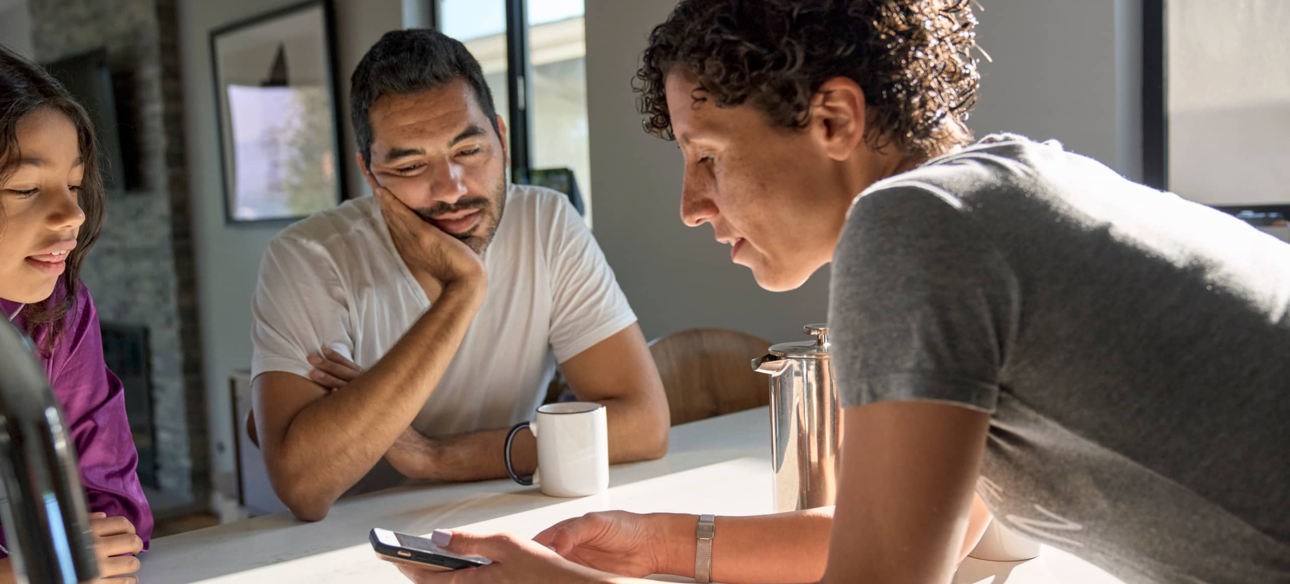Parents and their child checking something on the cell phone one of them is holding.