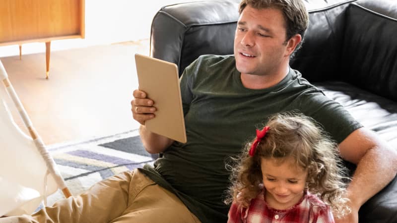 A parent learning about total parenteral nutrition on their tablet while their child plays beside them.