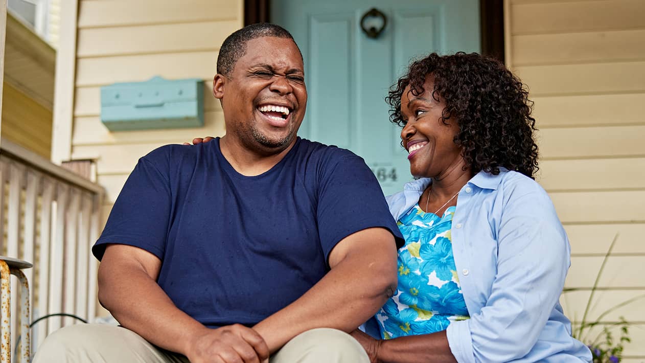 A couple laughing while waiting for a delivery on their front steps.