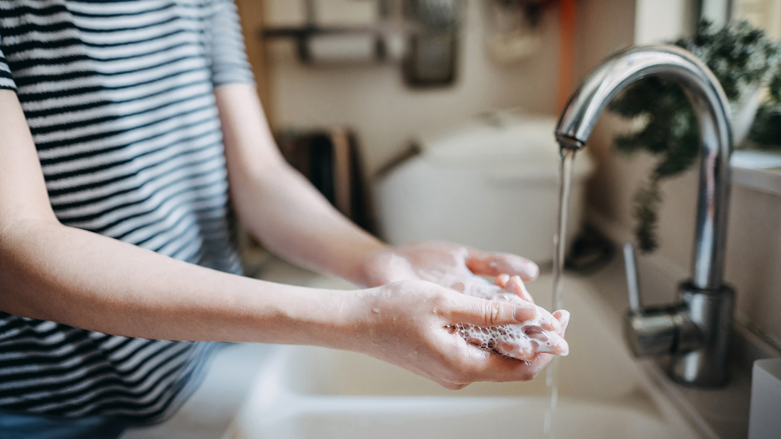 Individual washing hands with soap at a sink.