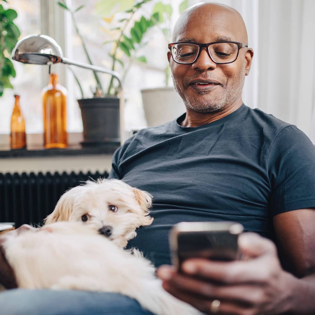 An older person with a dog on their lap, looking at their cell phone screen.