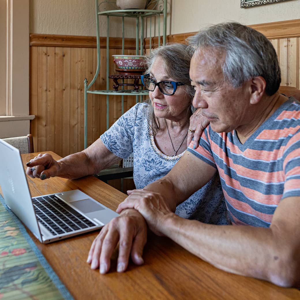 An older couple discussing something on their laptop screen.
