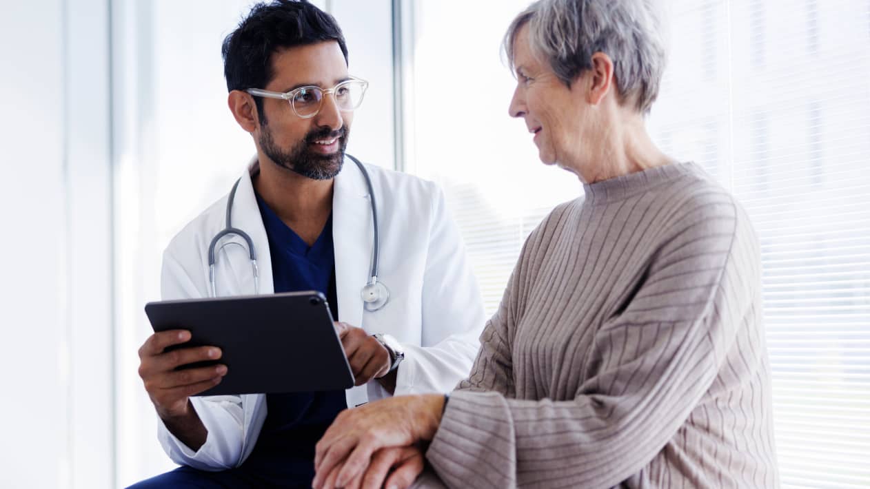 A practitioner holding a tablet as they talk with a patient