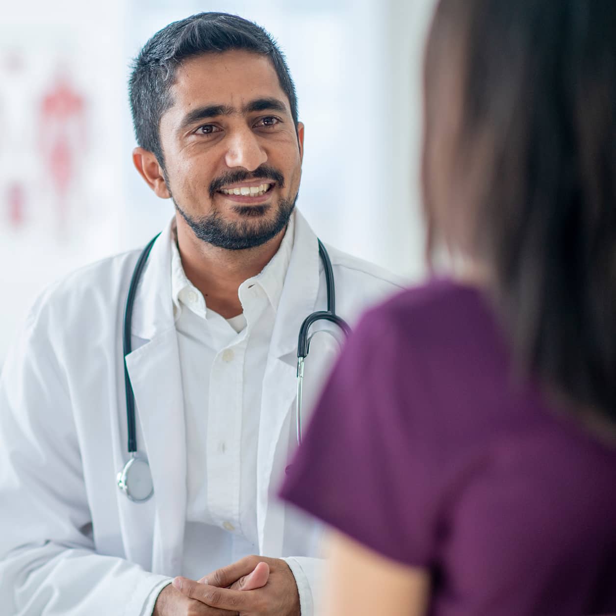 A practitioner wearing a stethoscope smiles at a patient