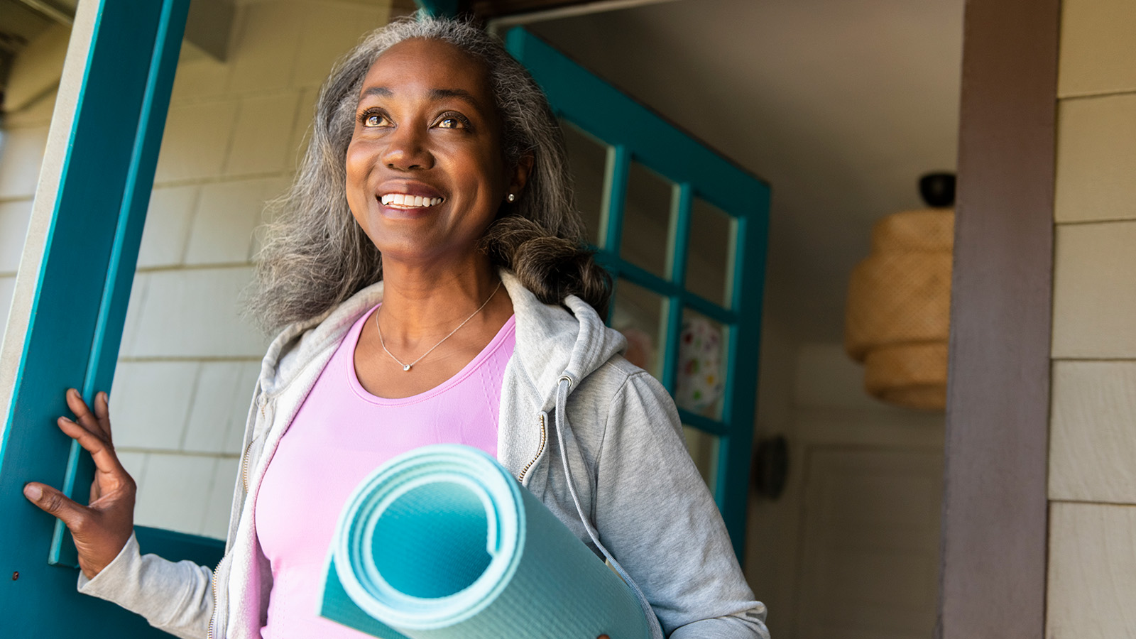 Woman leaving home with a yoga mat in hand.