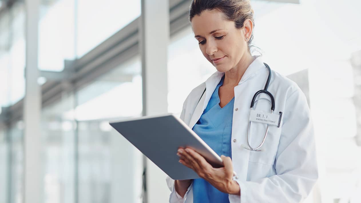 A practitioner looks down at a tablet screen in a hallway