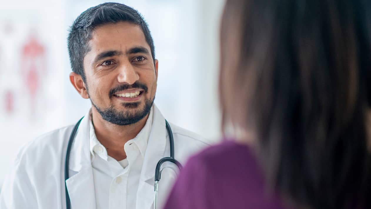 A practitioner wearing a stethoscope smiles at a patient