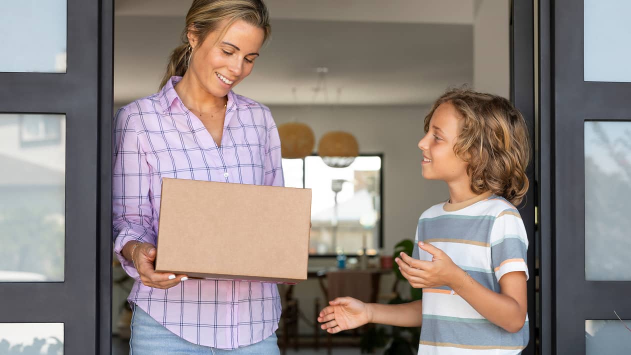 A parent picking up a delivery box as their child looks on
