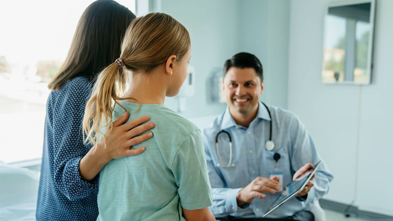 A CVS health care provider showing a tablet screen to a parent and their child in an exam room
