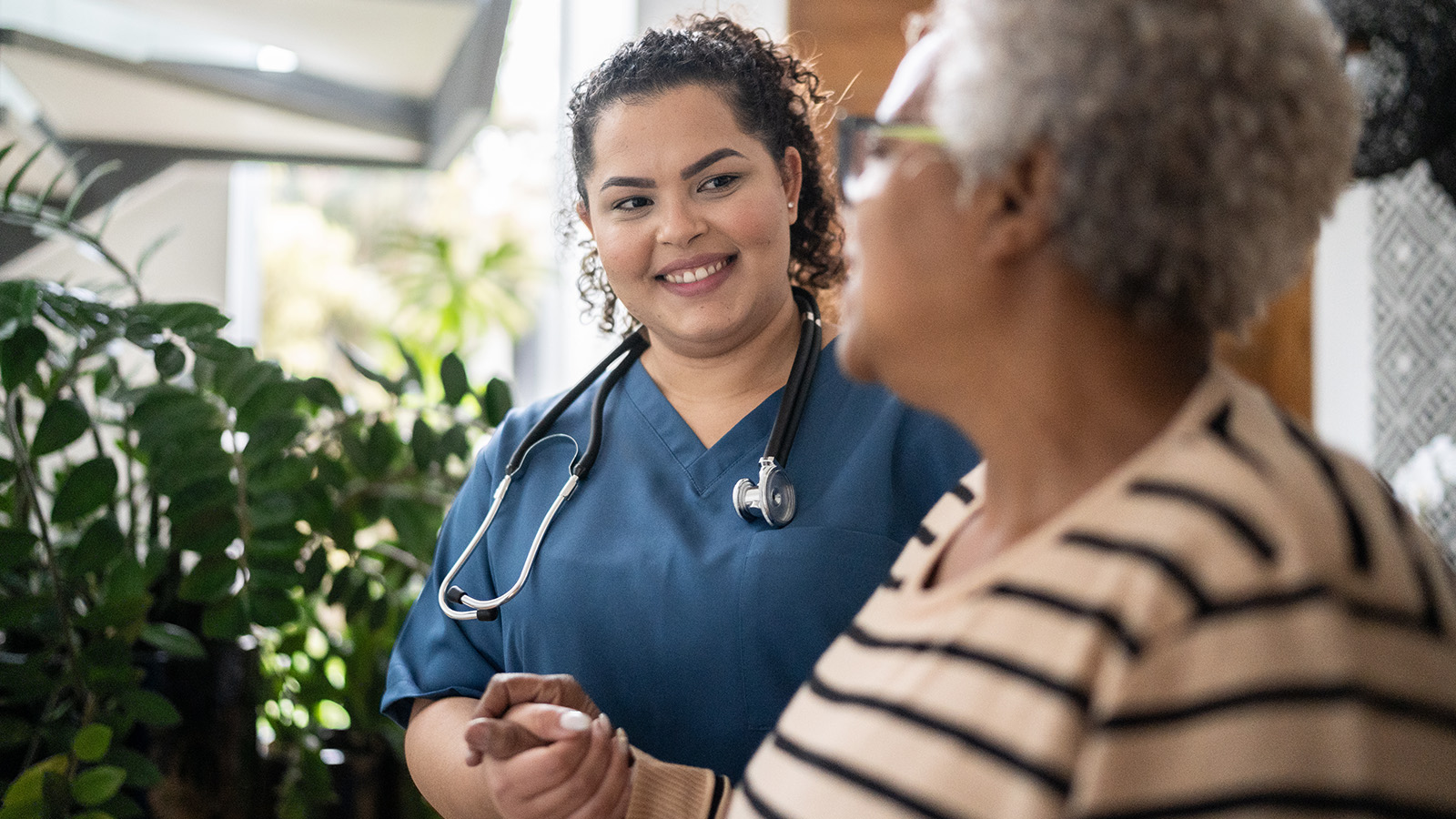A healthcare worker speaking with an elderly patient in a home setting.