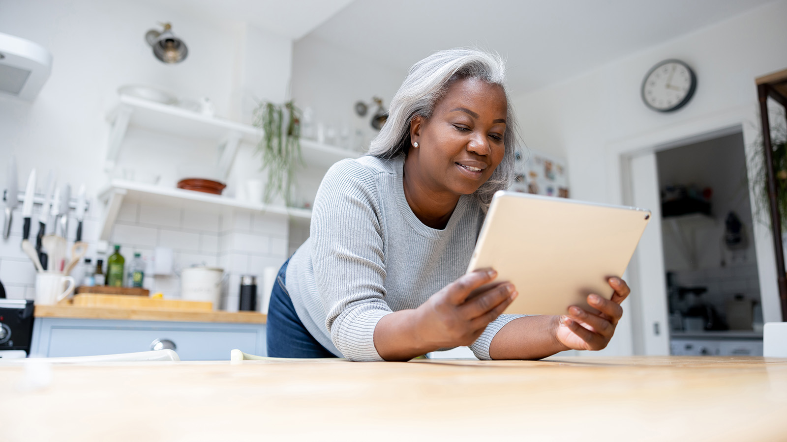 Person leaning over a table, holding a tablet in the kitchen.