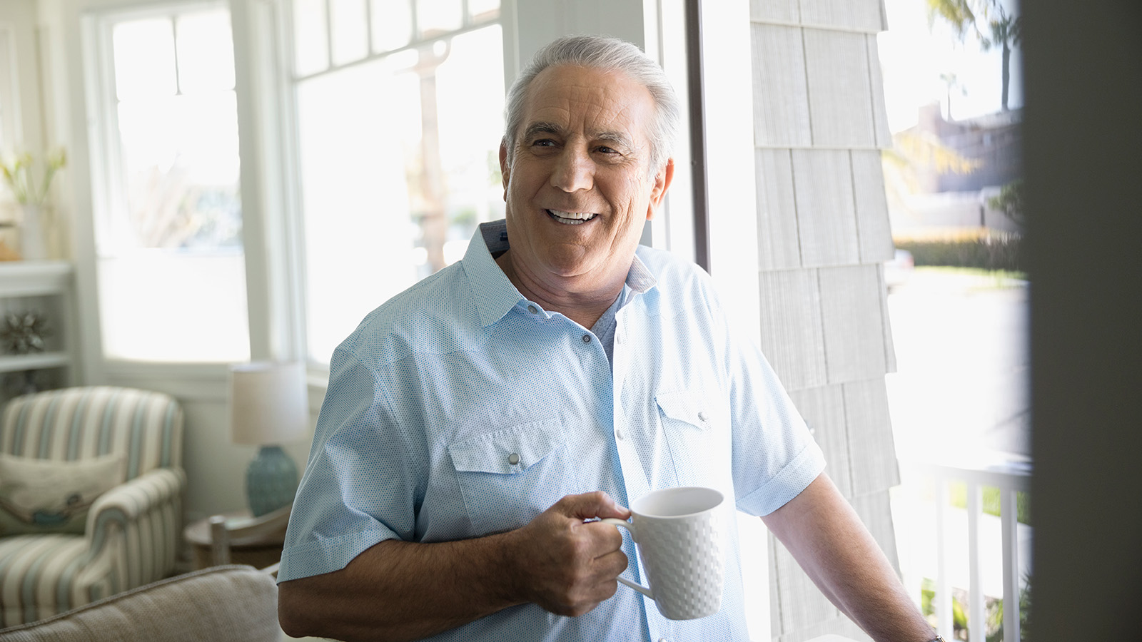 Man holding a coffee cup while looking out a window.