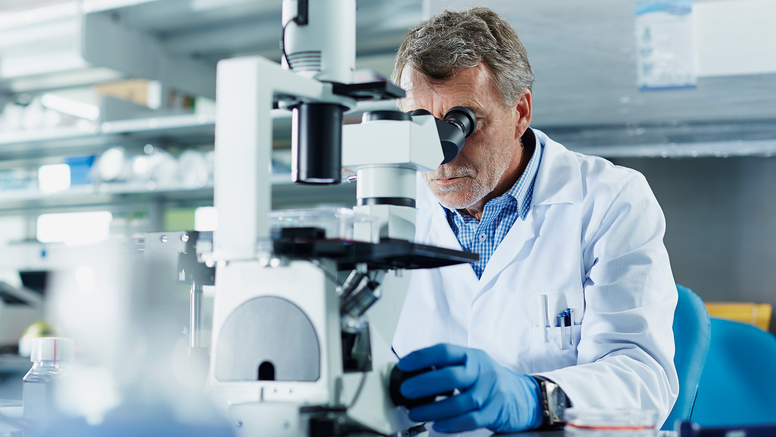 A man in a lab coat examines a sample under a microscope in a well-equipped laboratory.