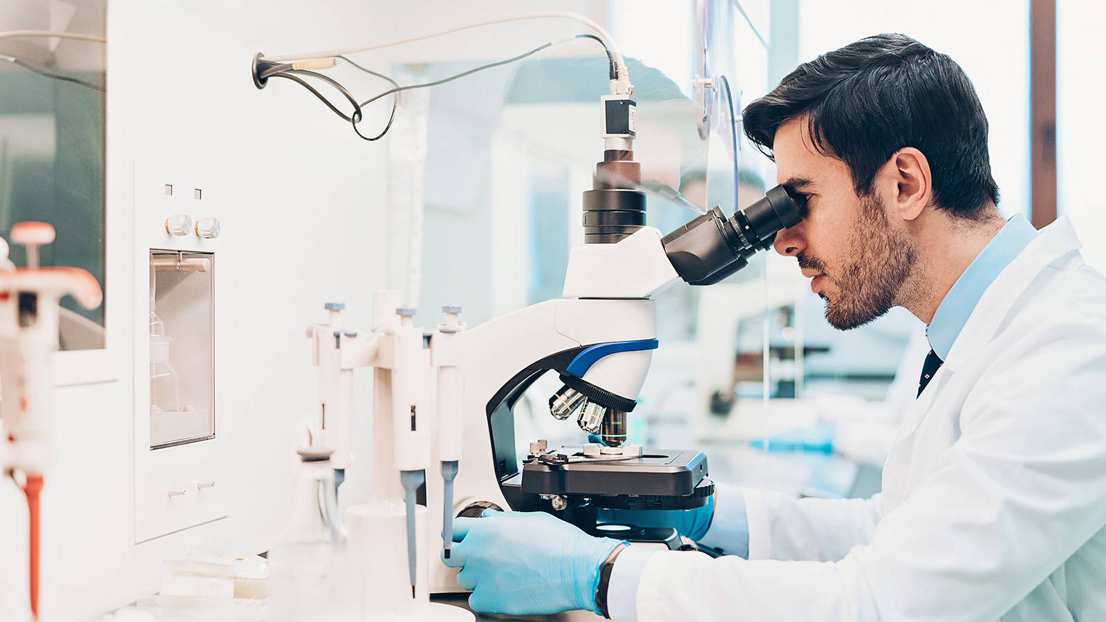 A healthcare professional examines a sample under a microscope in a laboratory, surrounded by scientific equipment and glassware.