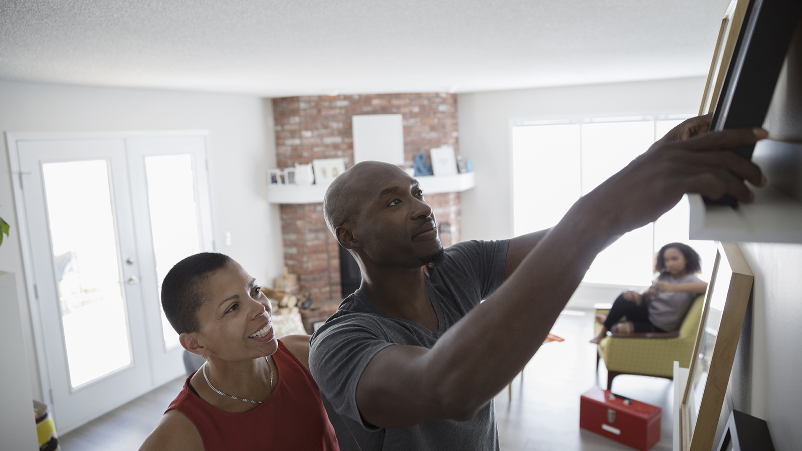 Two people arranging a picture frame on a wall in a living room