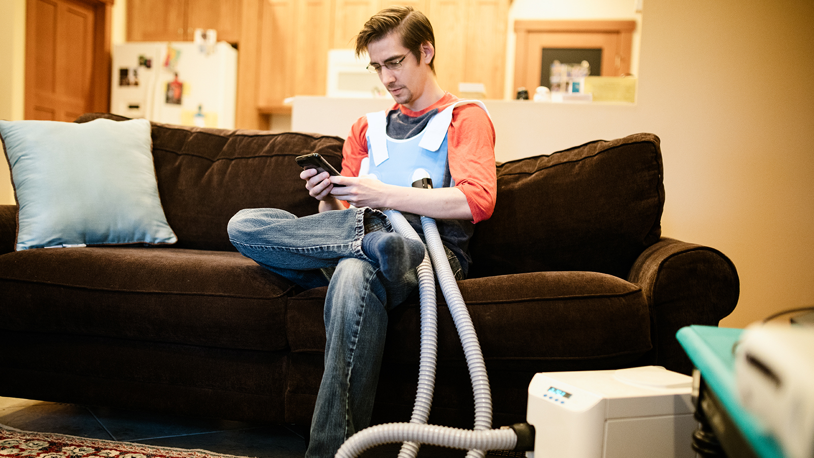 A person sitting on a couch using a phone with medical equipment attached