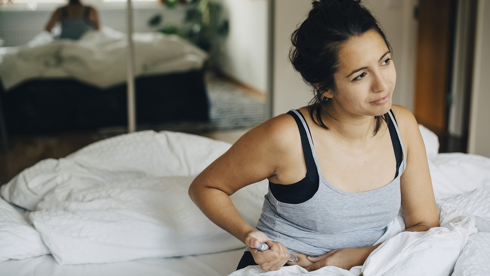 Woman administering medication to herself while sitting on a bed