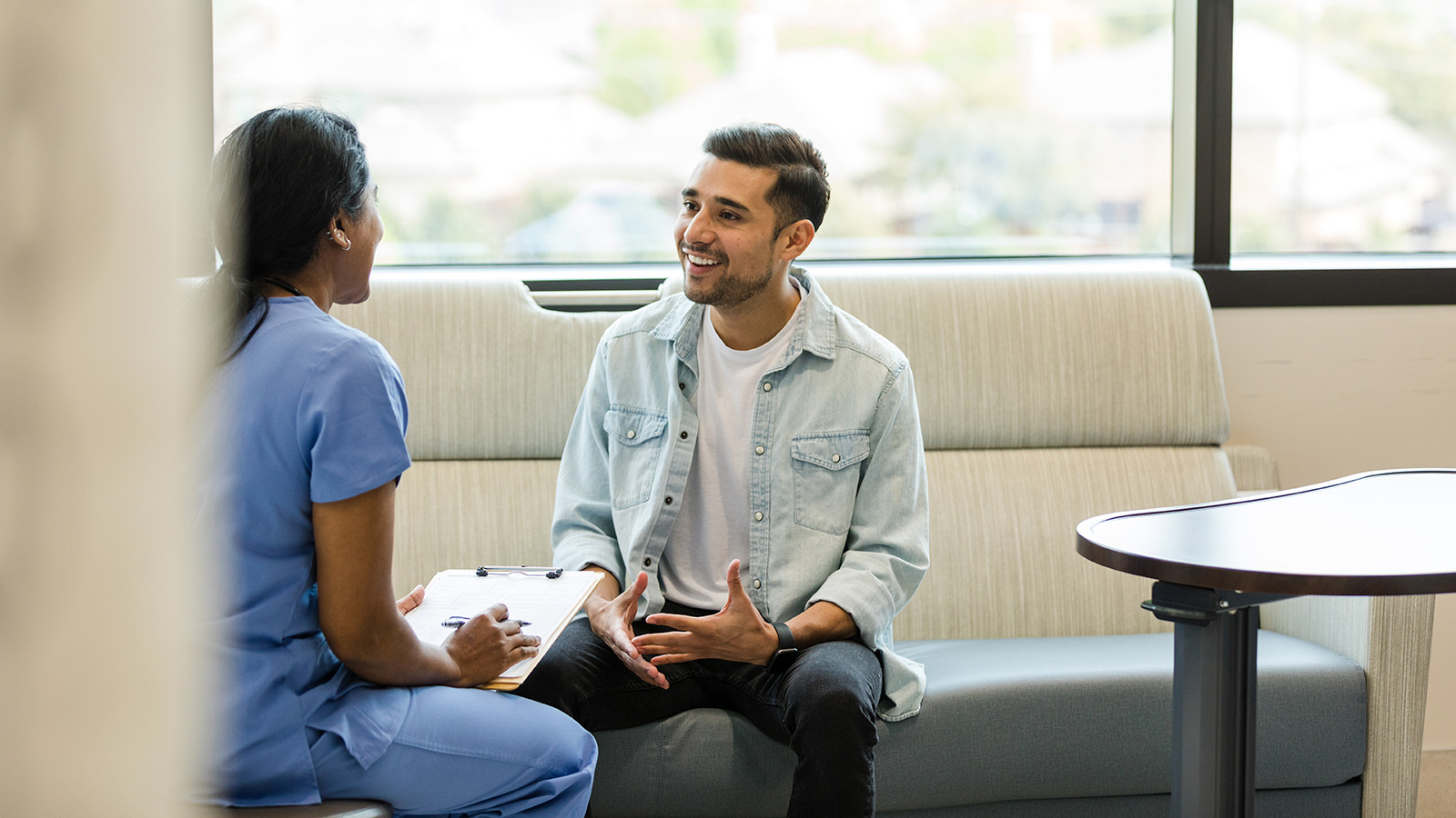 A healthcare worker engages with a young man in a casual setting, discussing health matters with a clipboard.
