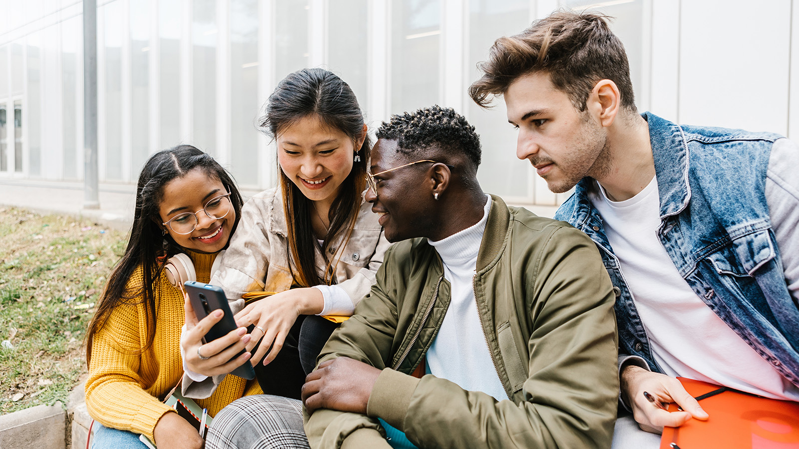 A group of four individuals sit together, focused on a smartphone, sharing a moment of connection and engagement.