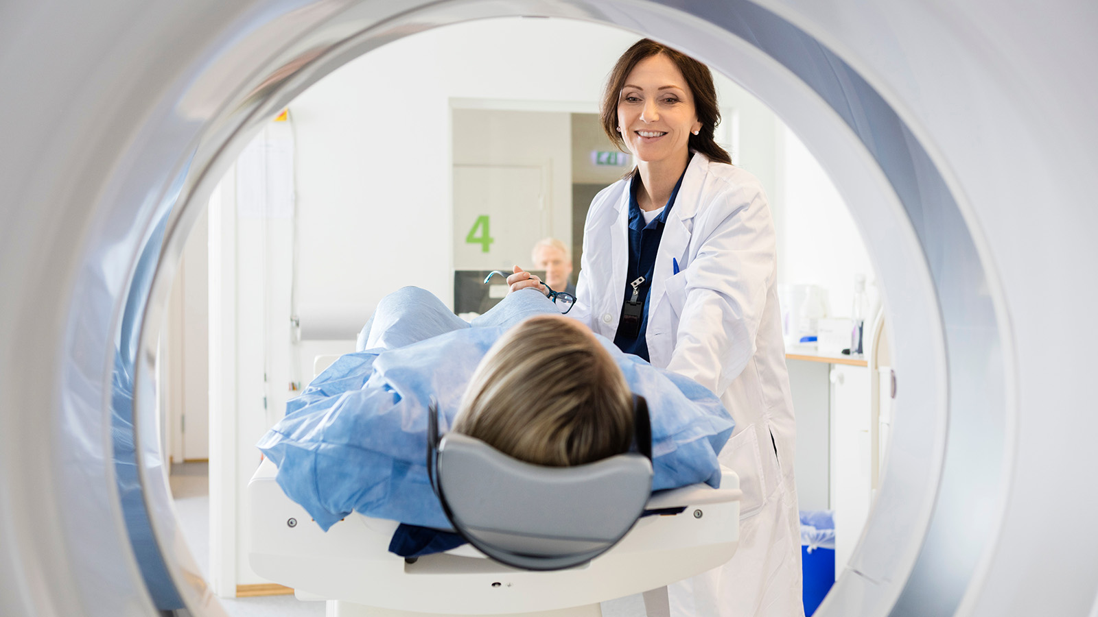 A medical professional assists a patient lying on a scanning table, preparing for a medical imaging procedure in a clinical setting.