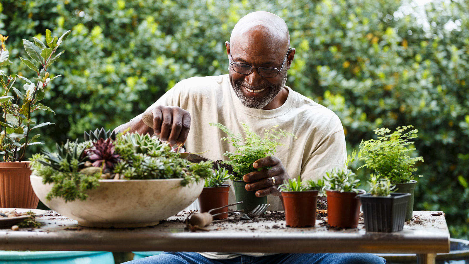 A person potting plants at a table in a garden.