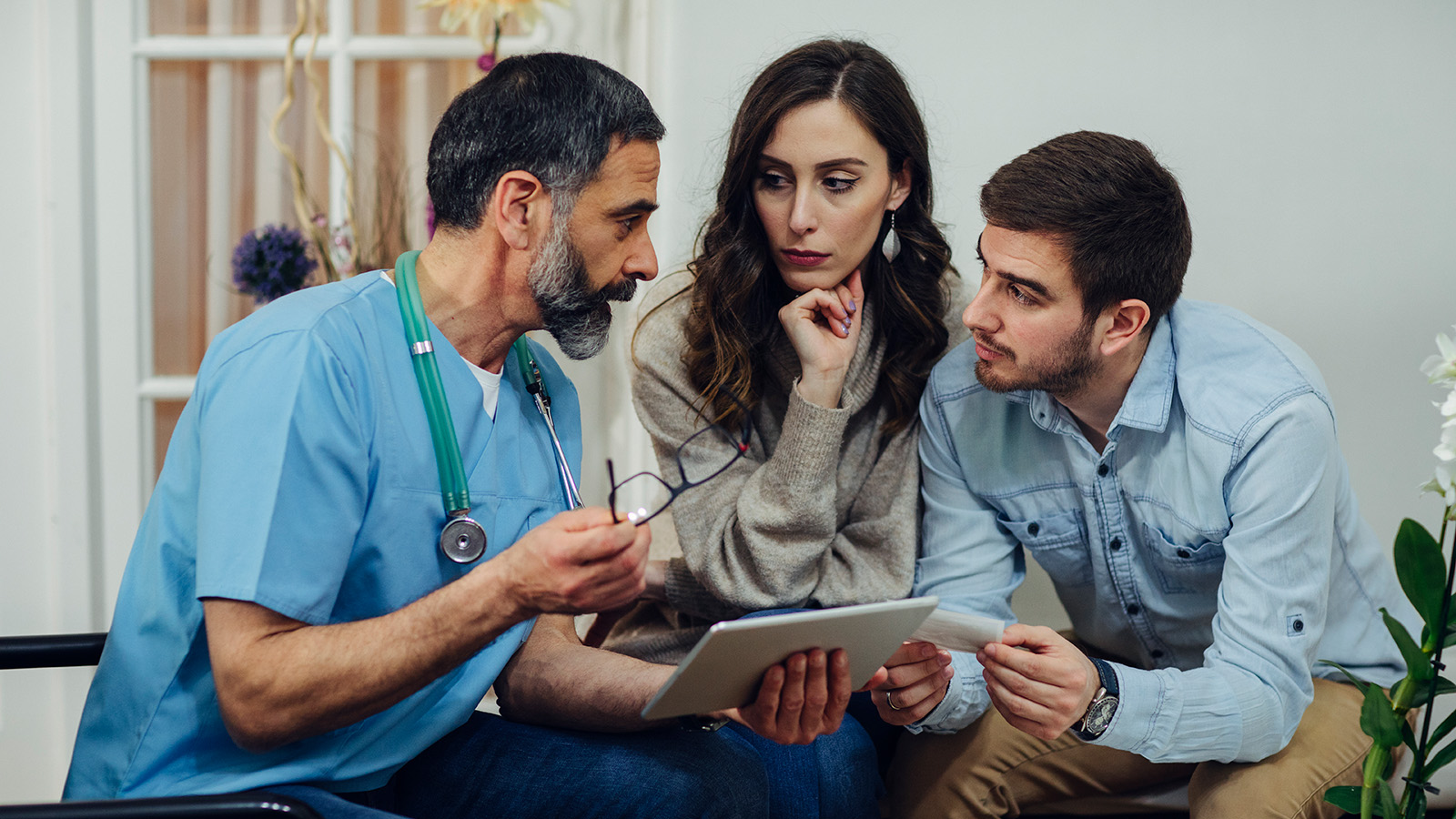 A doctor discusses information on a tablet with two individuals, conveying important medical details in a healthcare setting.