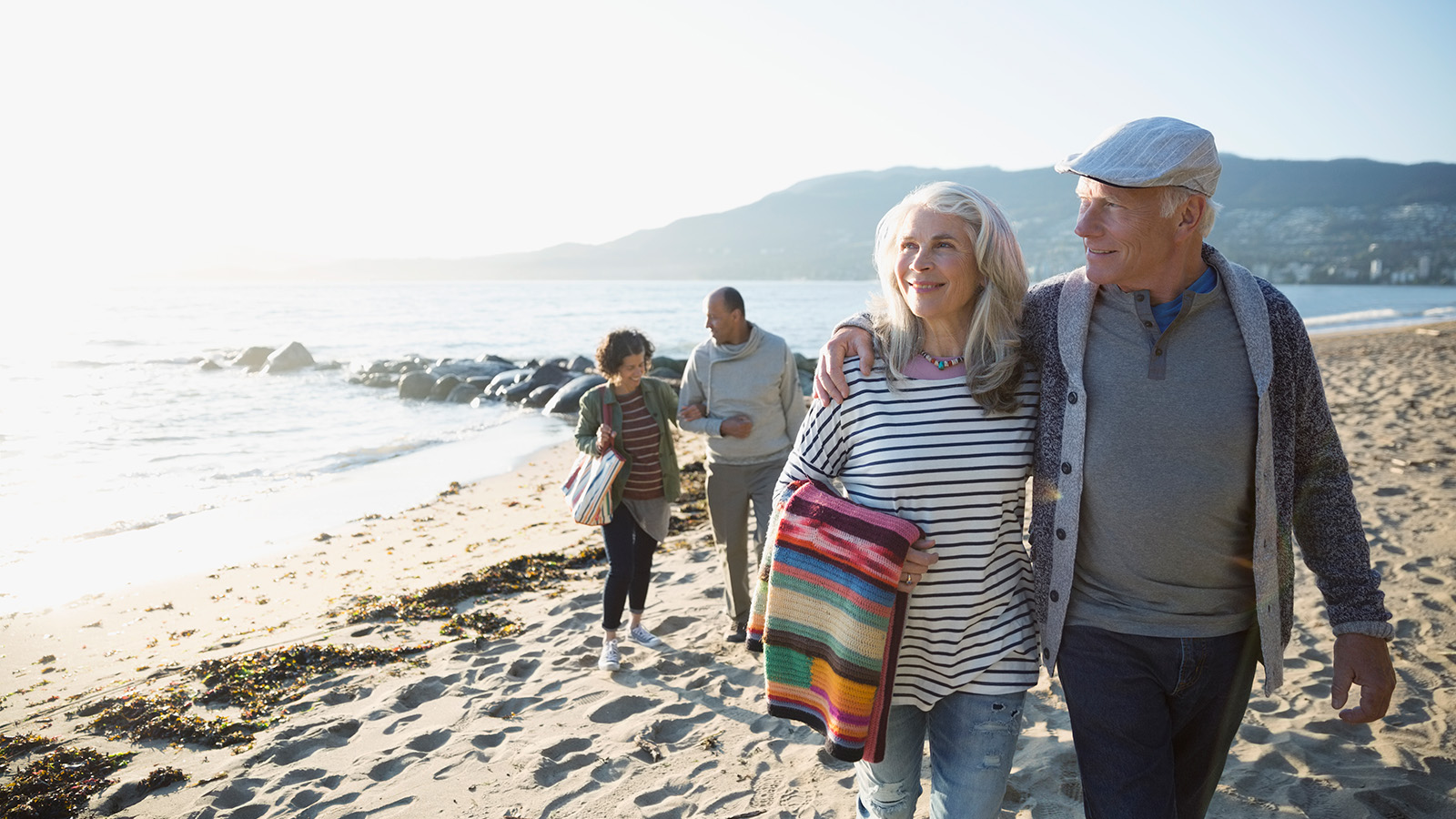 A group of people walking along a beach, with an elderly couple holding hands and enjoying the scenery.