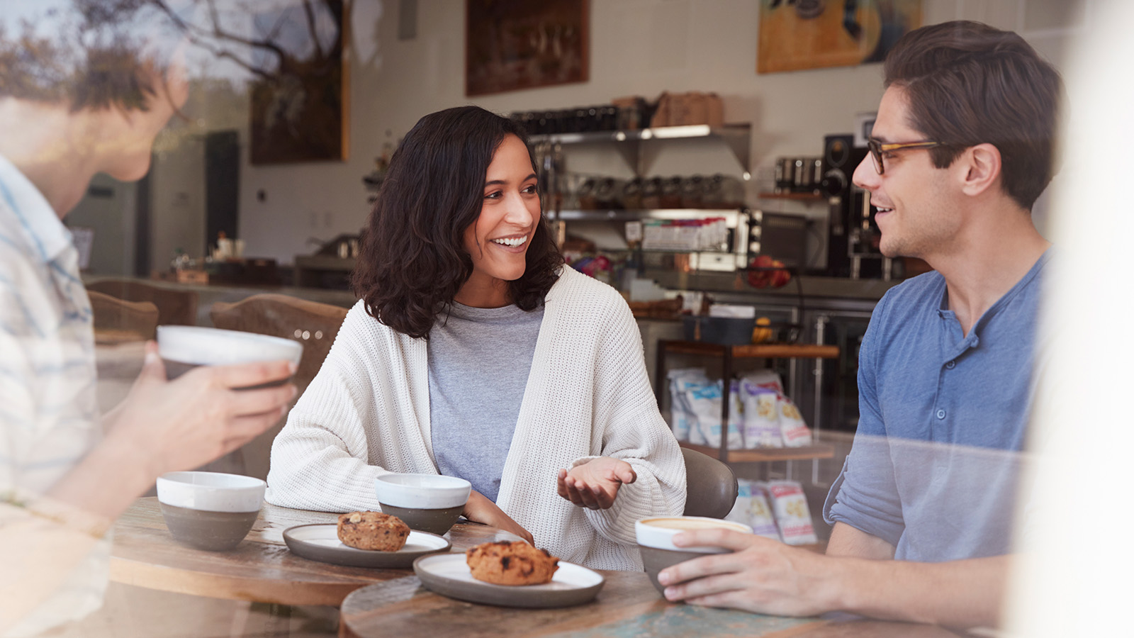 Three people sit at a café table, engaged in conversation, with bowls of food in front of them.