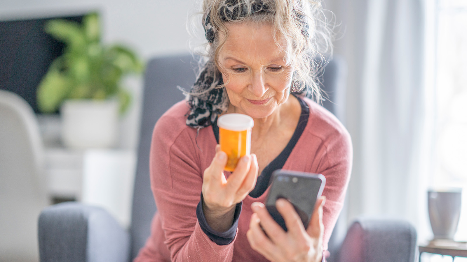 A woman holds a prescription bottle while looking at her phone