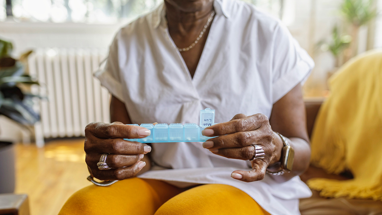 An elderly person holds a weekly pill organizer, preparing to take medication.