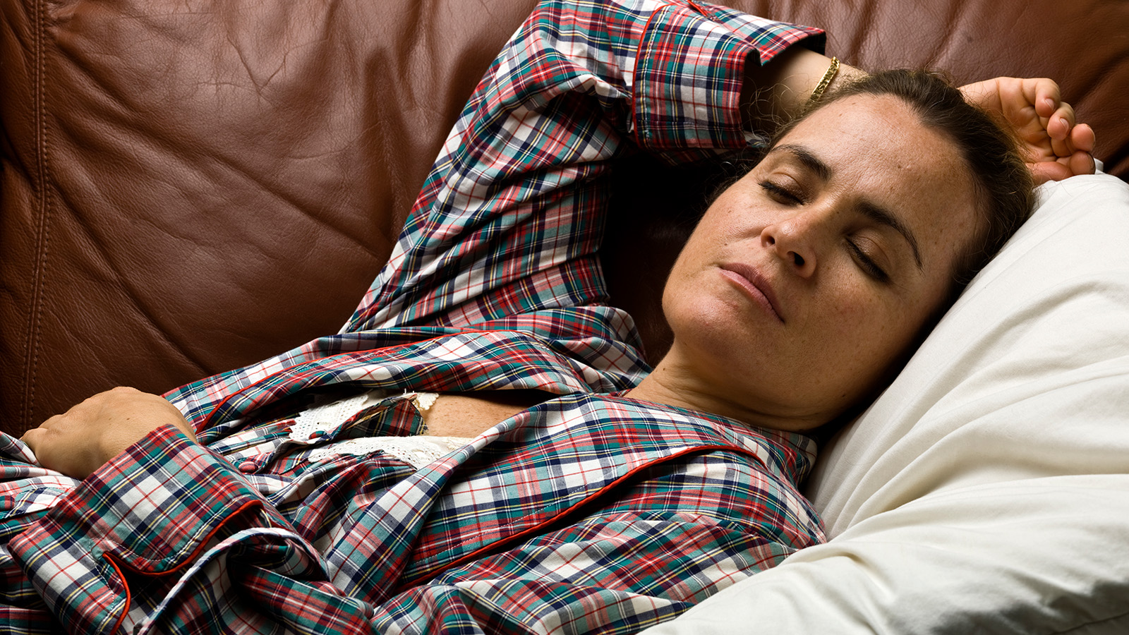A person lies on a couch, wearing plaid pajamas, appearing relaxed and resting comfortably.