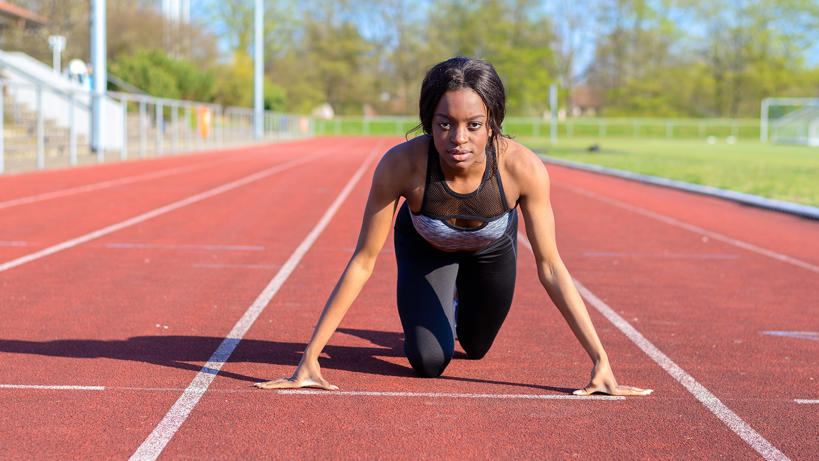 A woman prepares to run on a track, positioned in a starting stance, wearing athletic gear and focused on the race.