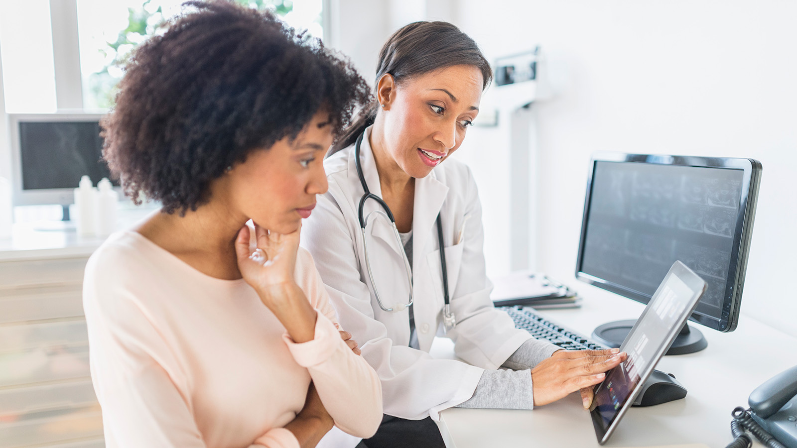 A doctor discusses information on a tablet with a patient in a medical office.