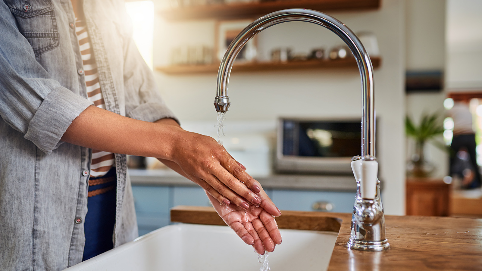 A person washes their hands under a faucet in a bright kitchen.