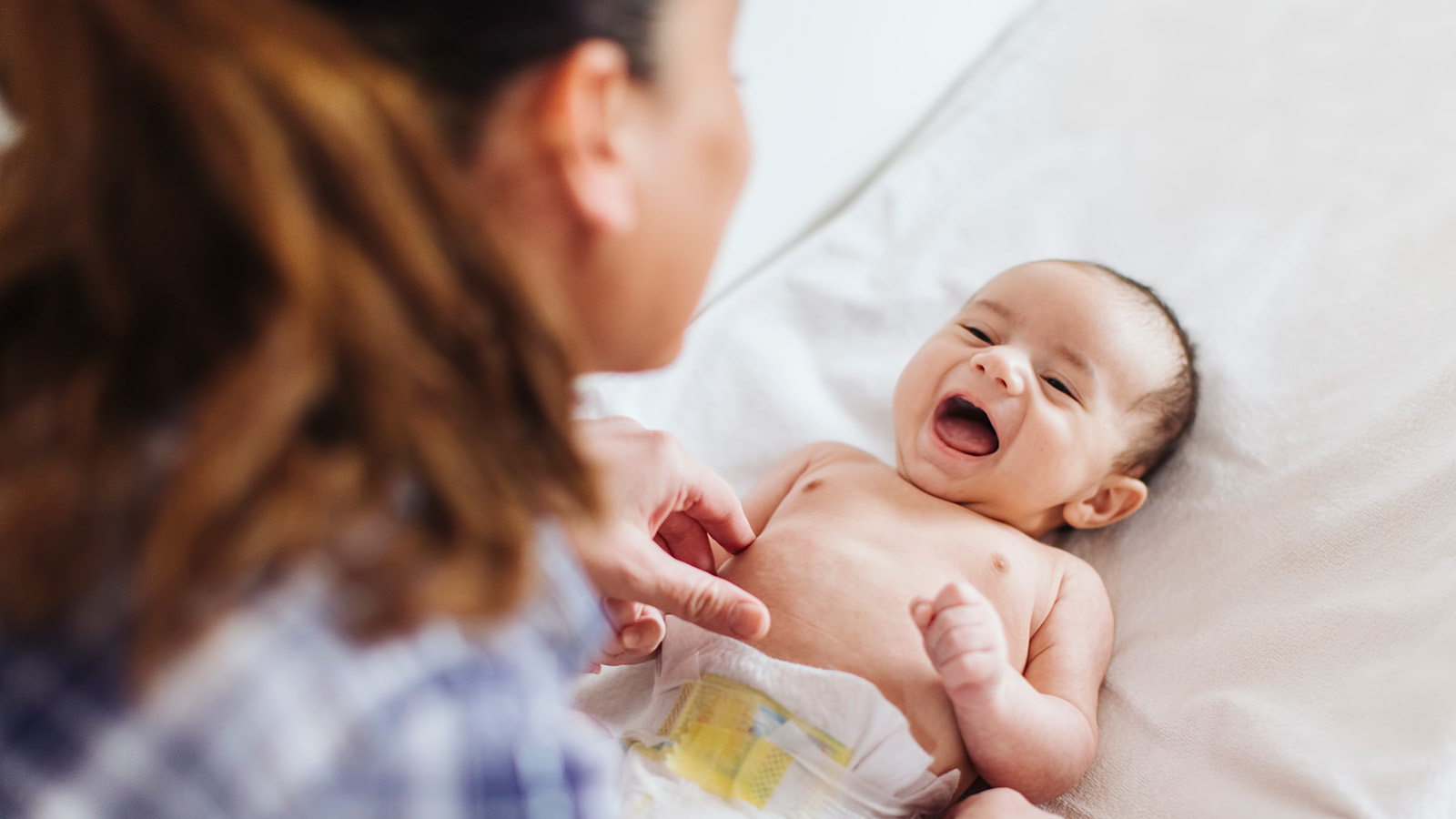 A caregiver gently examines a baby lying on a soft surface, focusing on the baby’s chest and diaper area.
