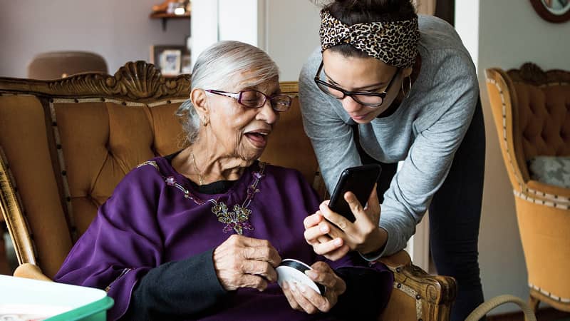An older woman being shown something on a cell phone screen by a family member.