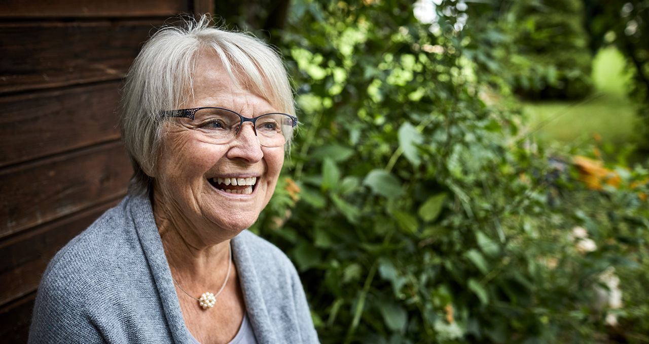 An older woman sitting outdoors surrounded by greenery